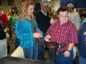 A teen assists a young man with Down Syndrome with showing a lamb at the fair